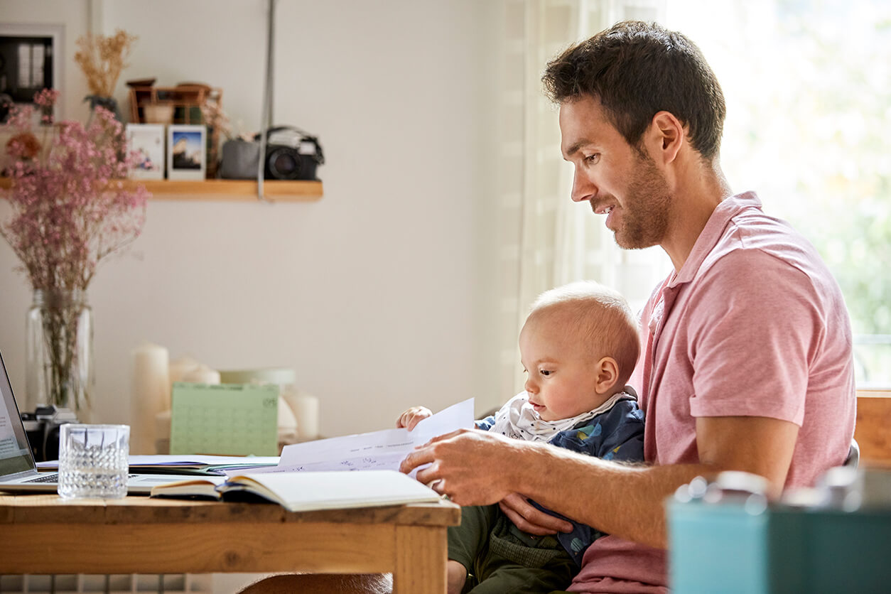 Man analyzing papers while holding son at table